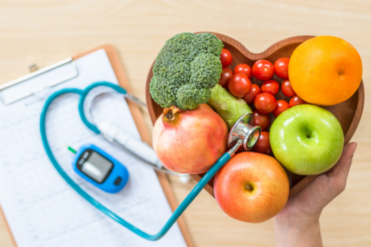 Frutta e verdura, fra cui i broccoli, che sono importanti per affrontare l'insulino resistenza. Le crucifere e gli altri ortaggi sono disposti in una ciotola a forma di cuore, accanto c'è uno stetoscopio e un guclometro. 