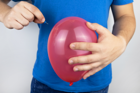 Uomo con maglia blu e un palloncino rosso in mano, simbolo del gonfiore addominale.